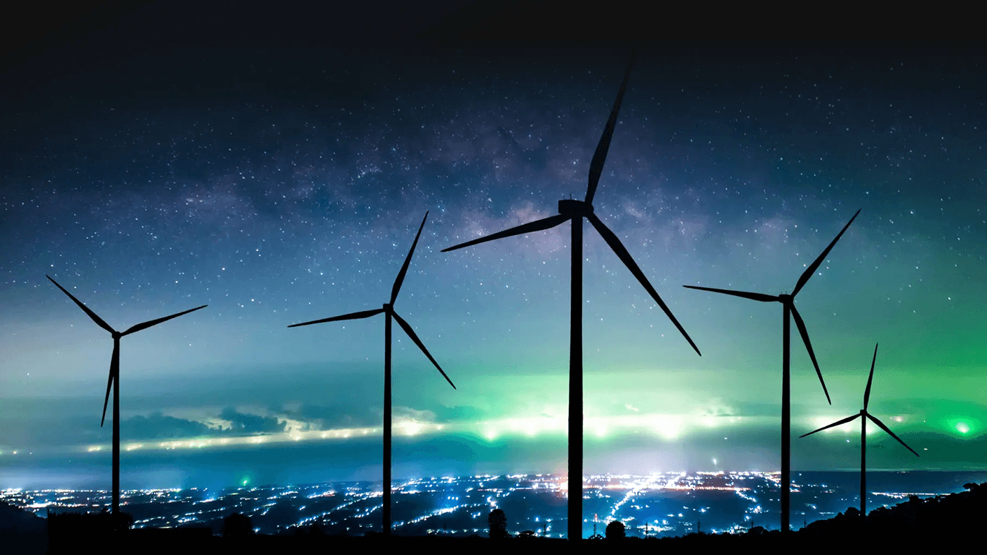 Nattebillede af vindmøller med oplyst by i baggrunden